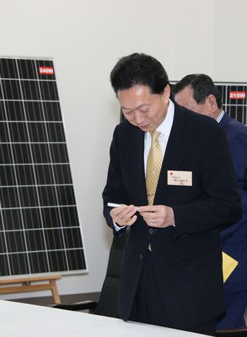 太陽光発電パネルを背に説明を聞く鳩山総理の写真