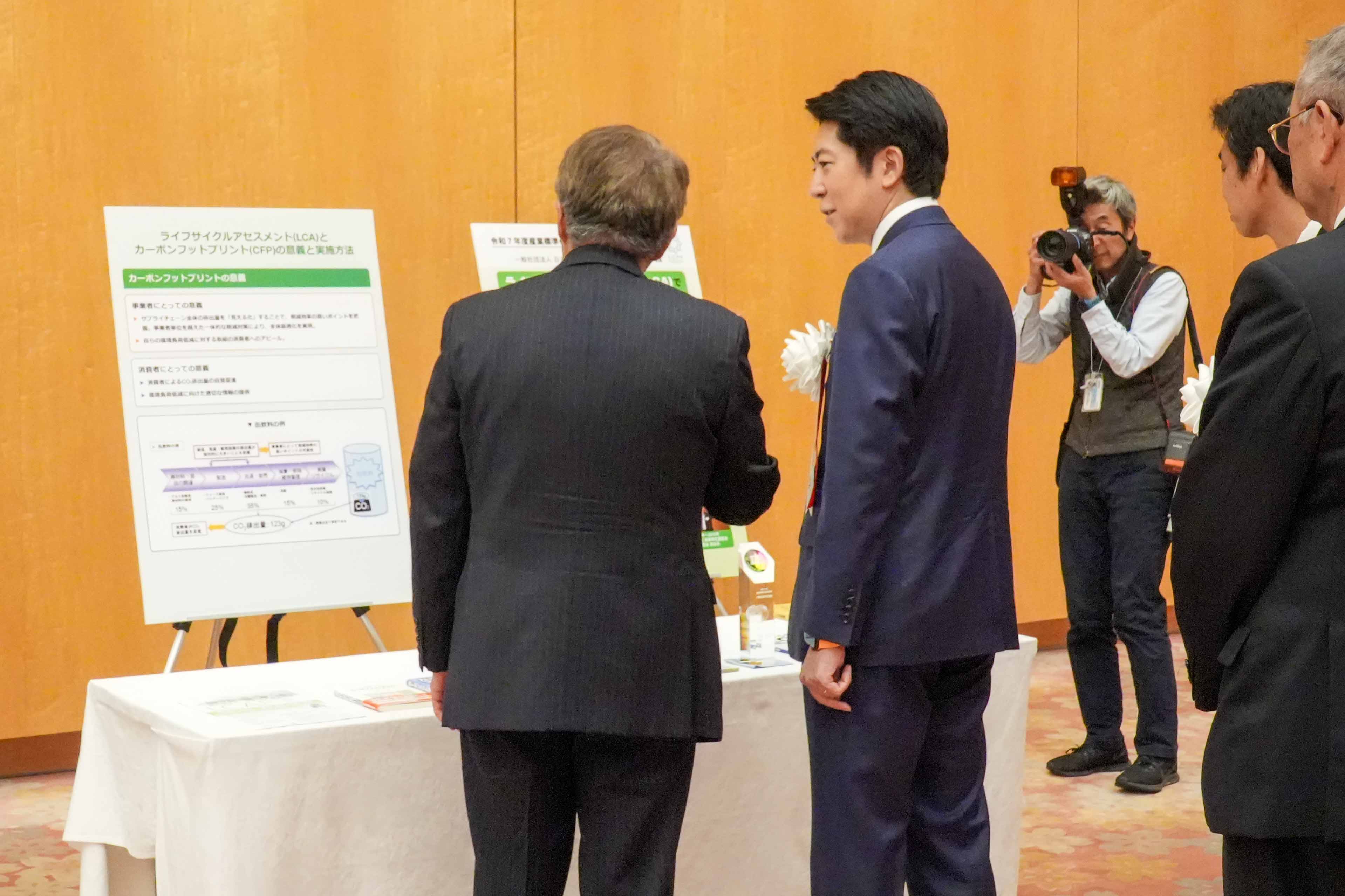 受賞者展示ブースを観覧する佐藤官房副長官１