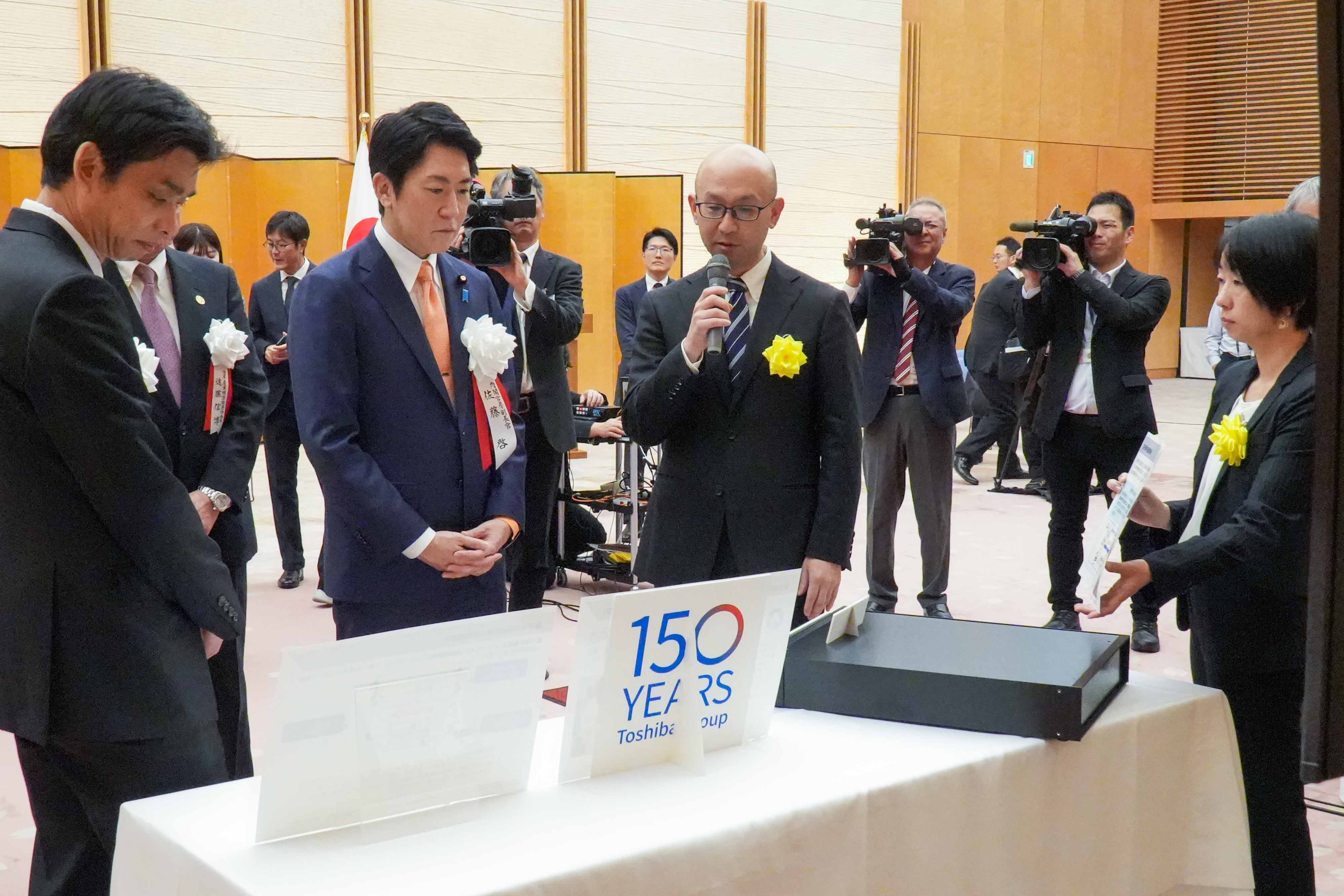 受賞者展示ブースを観覧する佐藤官房副長官２