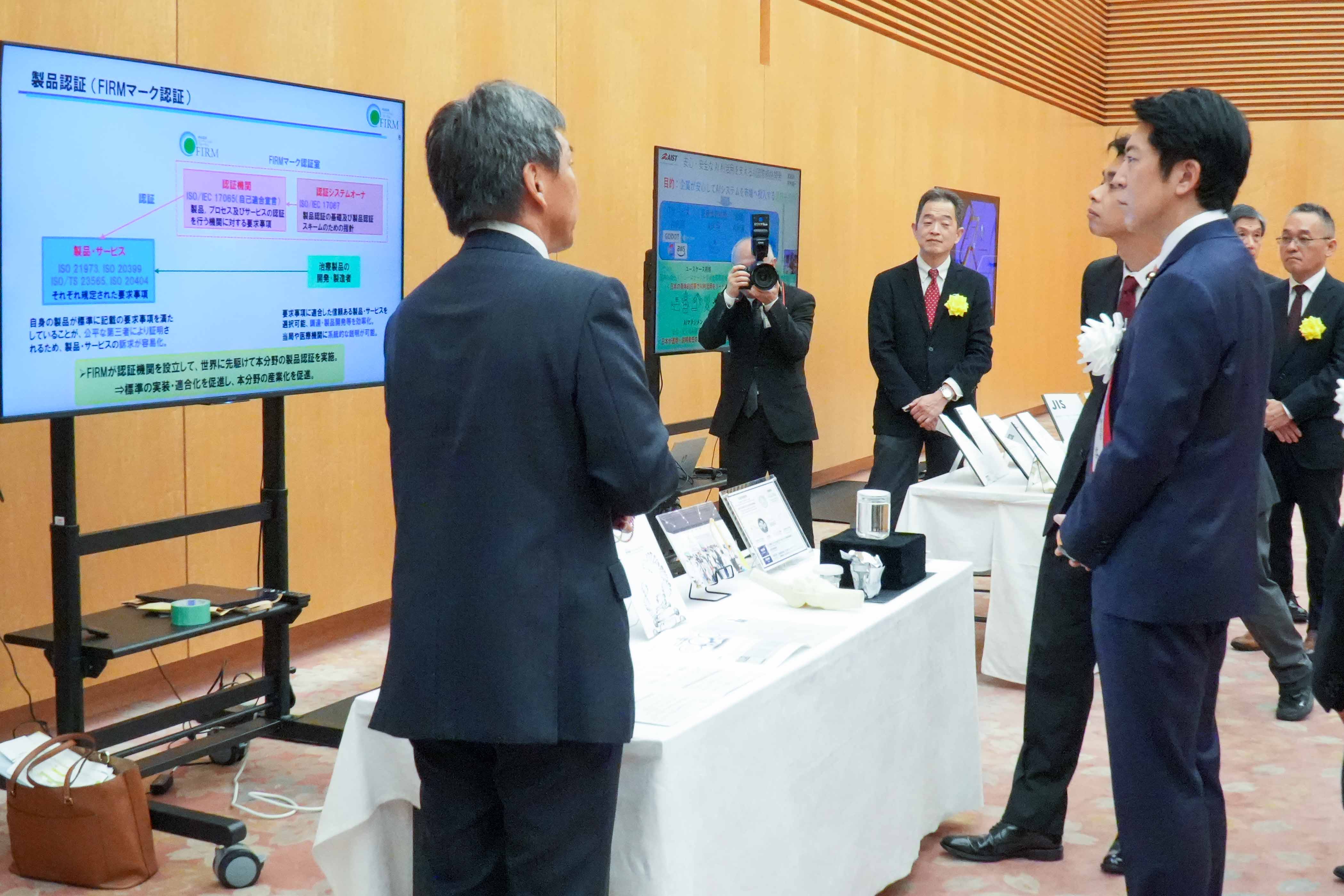 受賞者展示ブースを観覧する佐藤官房副長官４