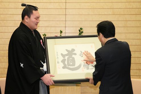 記念品の色紙に押された手形に手をあわせる菅総理